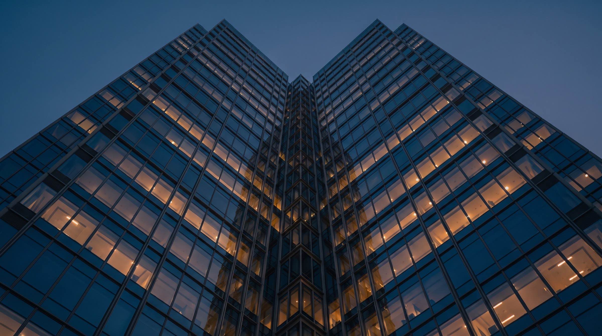 Glass facade of a tower at dusk, warm lit windows in a precise grid